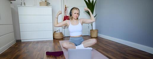 Porträt von jung sportlich Frau folgenden online Anleitung während Fitness trainieren, mit Laptop, Sitzung auf Yoga Matte foto