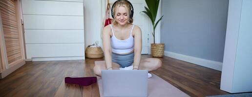 Porträt von jung sportlich Frau folgenden online Anleitung während Fitness trainieren, mit Laptop, Sitzung auf Yoga Matte foto