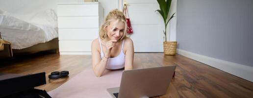 Porträt von schön blond Frau suchen beim Fitness Tutorials auf Laptop, Lügen auf Gummi Yoga Matte, folgenden trainieren Anleitung online foto