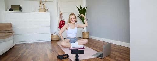 Porträt von jung weiblich Athlet, Fitness Trainer Aufzeichnung vlog, Ausbildung Session auf Digital Kamera, Sitzung im ein Zimmer auf Gummi Yoga Matte, zeigen Übungen foto