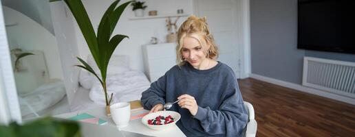 Porträt von jung offen Mädchen Aufpassen s auf Laptop, genießen Film und Essen im Vorderseite von Laptop, haben Frühstück und starren beim Bildschirm foto