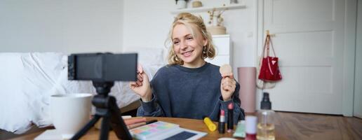 Porträt von jung Frau, Schönheit Inhalt Schöpfer, Sitzung im ein Zimmer im Vorderseite von Digital Kamera, Aufzeichnung bilden Lernprogramm vlog, zeigen kosmetisch Gesichts- Produkte foto