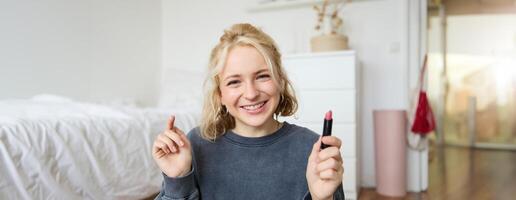 Porträt von Niedlich, charismatisch Schönheit Blogger, Frau sitzt im ein Zimmer mit Lippenstift im Hand, reden Über bilden, chatten mit Anhänger, Aufzeichnung online Strom auf Sozial Medien App foto