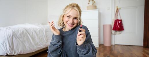 Porträt von Niedlich, charismatisch Schönheit Blogger, Frau sitzt im ein Zimmer mit Lippenstift im Hand, reden Über bilden, chatten mit Anhänger, Aufzeichnung online Strom auf Sozial Medien App foto