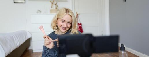 Porträt von Schönheit Blogger, Frau Aufzeichnungen auf Kamera im ihr Zimmer, zeigt an bilden Schönheit Produkte, Gespräche Über Kosmetika im vlog, macht Lebensstil Inhalt zum Anhänger auf Sozial Medien foto