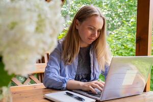 jung glücklich Frau fokussiert auf ihr Laptop im hölzern Alkoven. entspannt draussen Rahmen betont Komfort und Produktivität. Fernbedienung Arbeit Lernen Konzept foto