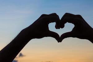 Liebe unterzeichnen. Herz Symbol durch Hand Silhouette im Sonnenuntergang Himmel. Jahrgang Stil. foto