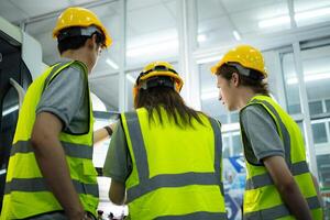 zurück Aussicht von Gruppe jung Fabrik Arbeiter tragen ein schwer Hut suchen beim ein Computer Bildschirm benutzt zu Steuerung Produktion. foto