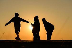 Kindersilhouette, die mit vielen Freunden Spaß macht und gegen den Sonnenuntergang spielt foto