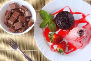 Kleine Torte mit Eis auf weißem Teller mit Erdbeeren über rustikalem Holztisch foto
