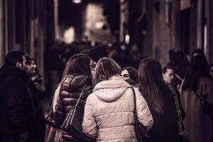 ferrara Italien 5 Februar 2023 ein Gruppe von jung Mädchen navigieren durch ein überfüllt Stadt Center beim Nacht umgeben durch historisch Gebäude foto