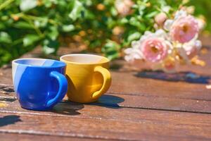 Tee Zeit. Kaffee Unterbrechung. Blau Gelb Tassen auf hölzern im Blühen Garten foto