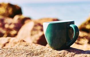 entspannen, ausruhen. Grün Keramik Tassen, Kaffee Tee Getränke auf ein Stein felsig Meer Bucht foto