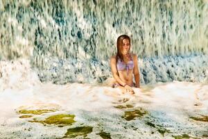 ziemlich Mädchen genießen Strom von Wasserfall im Schwimmen Schwimmbad beim Spa Resort foto