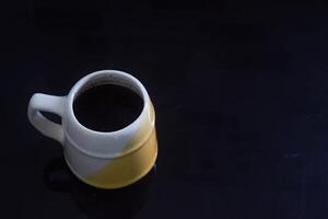 schwarz Kaffee im ein Weiß und Gelb Tasse auf ein schwarz Keramik Tabelle foto