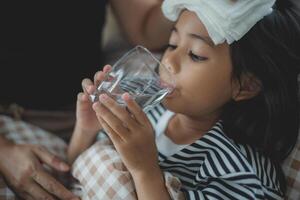 ein jung Mädchen ist Trinken Wasser während tragen ein Binde auf ihr Stirn foto