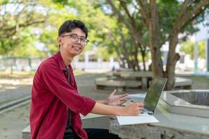 Porträt von asiatisch Hochschule Schüler mit Laptop suchen zu Kamera. ein Mann Arbeiten mit ein Laptop Computer beim Campus foto