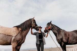 jung glücklich Frau im Hut mit ihr Pferd im Abend Sonnenuntergang Licht. draussen Fotografie mit Mode Modell- Mädchen. Lebensstil Stimmung. Konzept von draussen Reiten, Sport und Erholung. foto