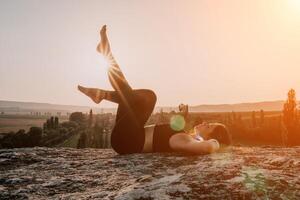 Fitness Frau. glücklich mittleren Alters Fitness Frau tun Dehnen und Pilates auf ein Felsen in der Nähe von Wald beim Sonnenuntergang. weiblich Fitness Yoga Routine. gesund Lebensstil mit Fokus auf Wohlbefinden und Entspannung. foto