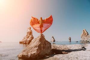 Frau Reise Meer. jung glücklich Frau im ein lange rot Kleid posieren auf ein Strand in der Nähe von das Meer auf Hintergrund von vulkanisch Felsen, mögen im Island, Teilen Reise Abenteuer Reise foto