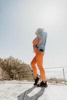 Fitness Frau Meer. glücklich Mitte alt Frau im Orange Sportbekleidung Übungen Morgen draußen auf Yoga Matte mit Laptop im Park Über Ozean Strand. weiblich Fitness Pilates Yoga Routine. gesund Lebensstil. foto