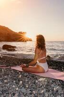 Frau Meer Yoga. glücklich Frau im Weiß Badeanzug und Boho Stil Armbänder üben draußen auf Yoga Matte durch Meer auf Sonnenuntergang. Frauen Yoga Fitness Routine. gesund Lebensstil, Harmonie und Meditation foto