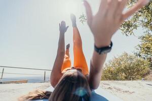 Fitness Frau Meer. glücklich Mitte alt Frau im Orange Sportbekleidung Übungen Morgen draußen auf Yoga Matte mit Laptop im Park Über Ozean Strand. weiblich Fitness Pilates Yoga Routine. gesund Lebensstil. foto