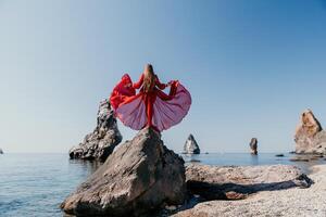 Frau Reise Meer. jung glücklich Frau im ein lange rot Kleid posieren auf ein Strand in der Nähe von das Meer auf Hintergrund von vulkanisch Felsen, mögen im Island, Teilen Reise Abenteuer Reise foto