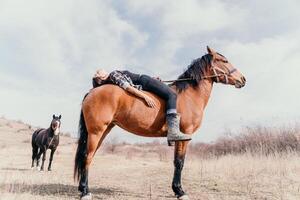 jung glücklich Frau im Hut mit ihr Pferd im Abend Sonnenuntergang Licht. draussen Fotografie mit Mode Modell- Mädchen. Lebensstil Stimmung. Konzept von draussen Reiten, Sport und Erholung. foto