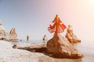 Frau Reise Meer. jung glücklich Frau im ein lange rot Kleid posieren auf ein Strand in der Nähe von das Meer auf Hintergrund von vulkanisch Felsen, mögen im Island, Teilen Reise Abenteuer Reise foto