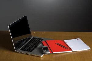Telefon, Laptop und leeres Notebook auf dem Schreibtisch foto