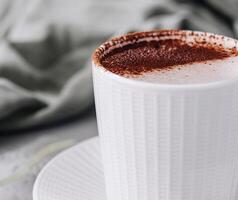 frisch Cappuccino im ein Weiß Tasse auf ein grau Oberfläche foto