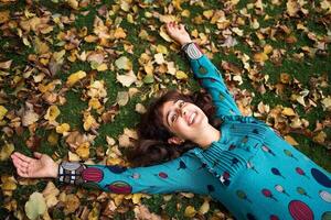 ein Mädchen im ein Kleid mit Luftballons Lügen auf das Boden bedeckt mit Herbst Blätter foto