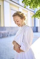 elegant Mitte Alter Frau im ein Weiß Jahrgang Kleid gegen das Hintergrund von historisch Gebäude im das Morgen Licht foto