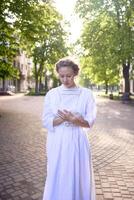 schick Mitte Alter Frau im ein Weiß Jahrgang Kleid im ein sonnendurchflutet Gasse foto