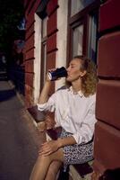 Mitte Alter Frau im 70er, 80er Jahre Stil Kleider mit ein Kaffee beflecken auf ihr Hemd Getränke Kaffee Sitzung auf das Fensterbrett foto