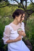 schön Frau im Weiß Jahrgang Kleid mit Zug und halten Jahrgang Spiegel im Frühling Garten beim Sonnenuntergang foto