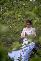 ein schön Frau im ein Weiß Jahrgang Kleid mit ein Zug ist beten während Sitzung auf ein gefallen Baum foto