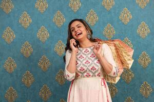 ein modisch Frau ist Lachen während reden auf das Telefon und halten Einkaufen Taschen foto