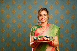 ein nett Frau im ein traditionell indisch Saree halten ein Tablett von diyas im ein Lager fotografieren während das Feier von Diwali foto