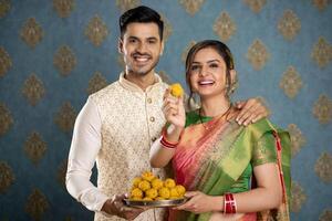 ein neu verheiratet Paar im traditionell Kleidung halten Teller von laddu während Diwali Festival foto