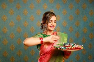 ein gut aussehend Frau im traditionell indisch Kleidung hält ein Teller von diyas während das Feier von Diwali foto