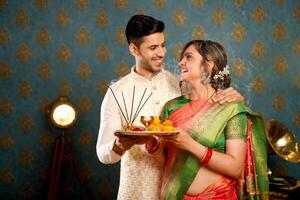 großartig Paar im traditionell indisch Kleidung halten pooja Teller im ihr Hände während suchen beim einer Ein weiterer foto