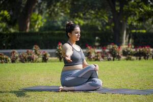 weiblich Fitness Lehrer Sitzung im sitzend mit gekreuzten Beinen Yoga Pose während üben Übung im Park. foto