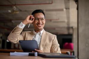 glücklich asiatisch Geschäftsmann lächelt während halten ein Digital Tablette und passt sich an seine Brille mit einer Hand. foto