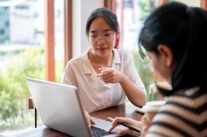 zwei jung asiatisch weiblich Hochschule Studenten sind Arbeiten auf ein Projekt zusammen, Treffen beim ein Kaffee Geschäft. foto