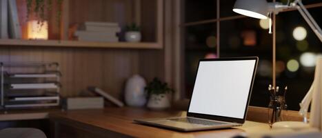 modern und gemütlich Zuhause Büro Arbeitsplatz beim Nacht mit ein weißer Bildschirm Laptop Computer auf ein Holz Tisch. foto