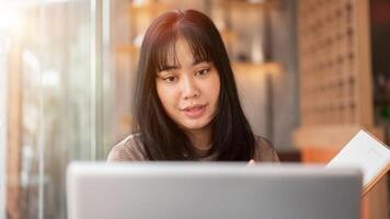 ein schön asiatisch Frau ist Arbeiten entfernt beim ein Cafe, Fokussierung auf ihr Laptop Computer. foto