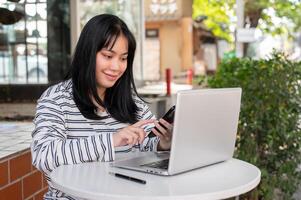 ein positiv asiatisch Frau ist reagieren zu Mitteilungen auf ihr Telefon während Arbeiten entfernt beim ein Cafe. foto