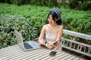 ein Frau Arbeiten entfernt im ein Garten, nehmen Anmerkungen im ihr Buch und Arbeiten auf ihr Laptop Computer. foto